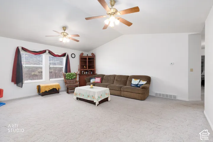 Living area featuring vaulted ceilings, dual ceiling fans with integrated lighting, neutral carpeting, and dual-pane windows