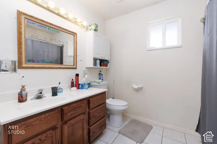 Bathroom featuring a wood-finish vanity with a white countertop, wall-mounted storage cabinetry, a multi-bulb light fixture, and tile flooring