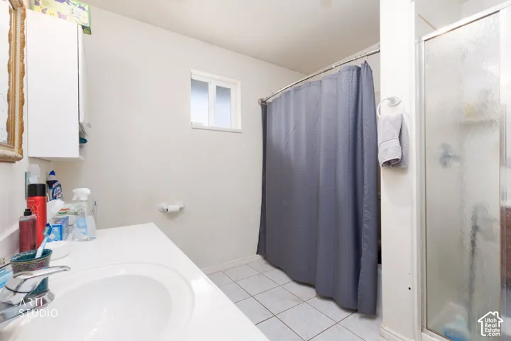 Bathroom featuring a vanity with a white countertop and integrated sink, tiled flooring, a shower-tub combination with a glass enclosure, and a wall-mounted storage cabinet