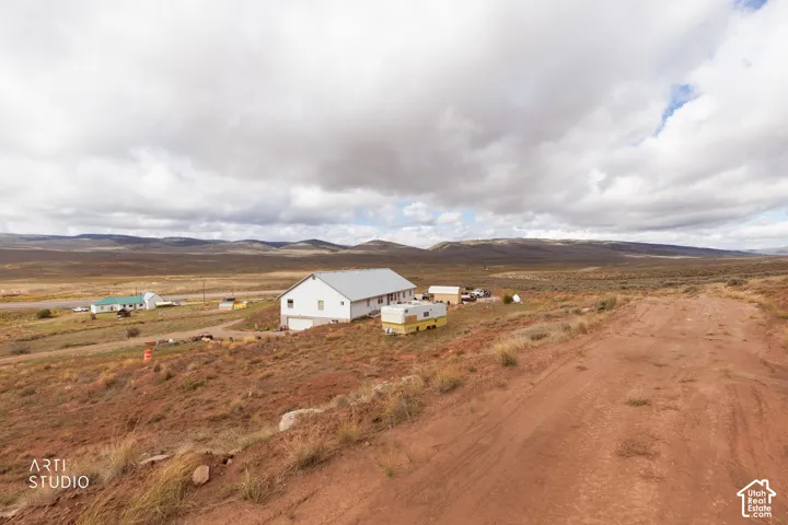 Single-story residence featuring a metal roof, light-colored siding, and a multi-car garage, set on an expansive lot with mountainous terrain