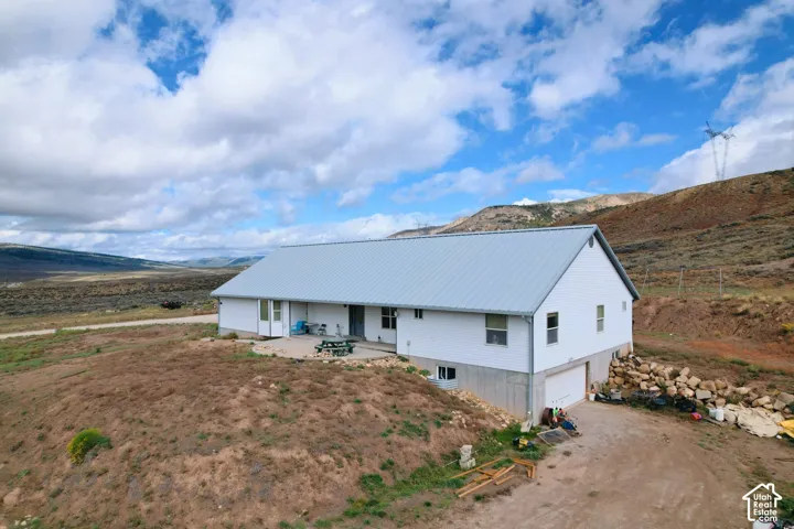 Single-level residence featuring a metal roof, white siding, concrete lower foundation, attached garage, and a circular concrete patio