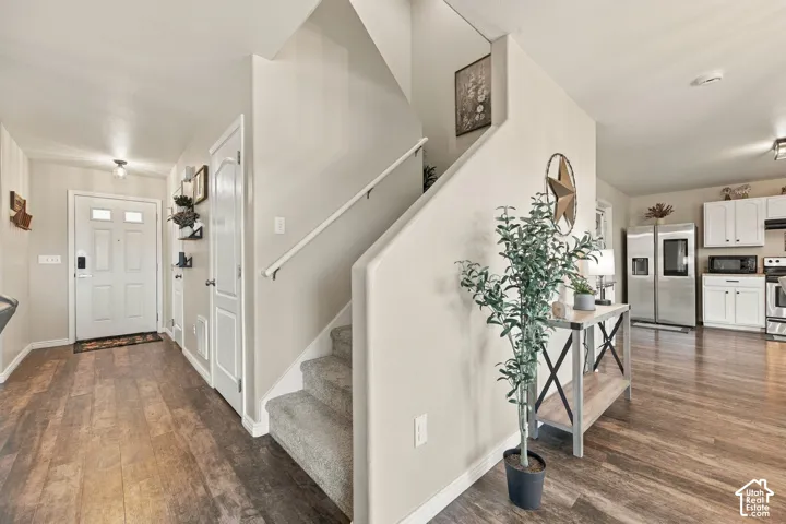 Entryway featuring wood-finish flooring, a staircase with carpeted treads and a painted railing, and white interior doors