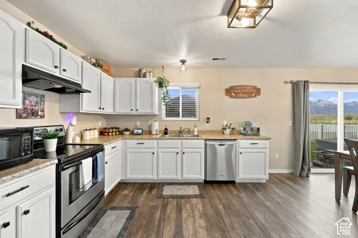 Kitchen featuring white shaker-style cabinetry, stone-finish countertops, stainless steel appliances, wood-finish flooring, and sliding glass door access