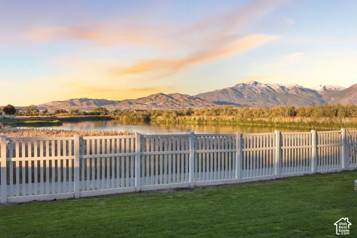 Backyard featuring a white vinyl picket fence, manicured lawn, water feature, and mountain backdrop