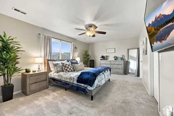 Neutral-toned bedroom featuring carpeting, a multi-blade ceiling fan with integrated lighting, and a large window