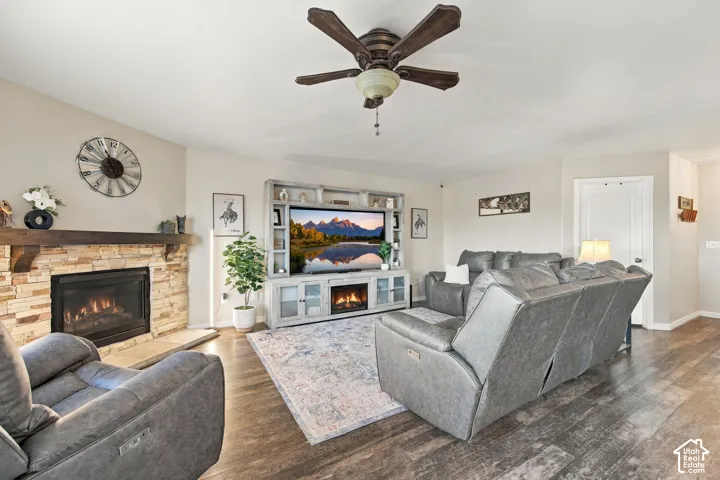 Floor-to-ceiling stone fireplace with a thick timber mantel, built-in media cabinetry, wood-finish flooring, and a multi-blade ceiling fan with integrated lighting