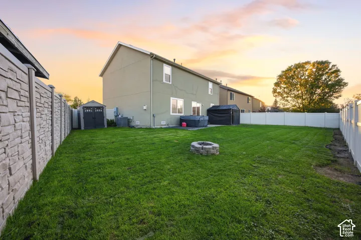 Fenced backyard featuring a stone-textured boundary wall, a central circular stone fire pit, and a concrete patio