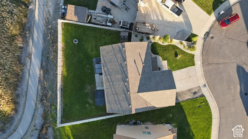 Aerial perspective featuring a shingled roof, fenced rear yard with lawn, concrete driveway, and established landscaping