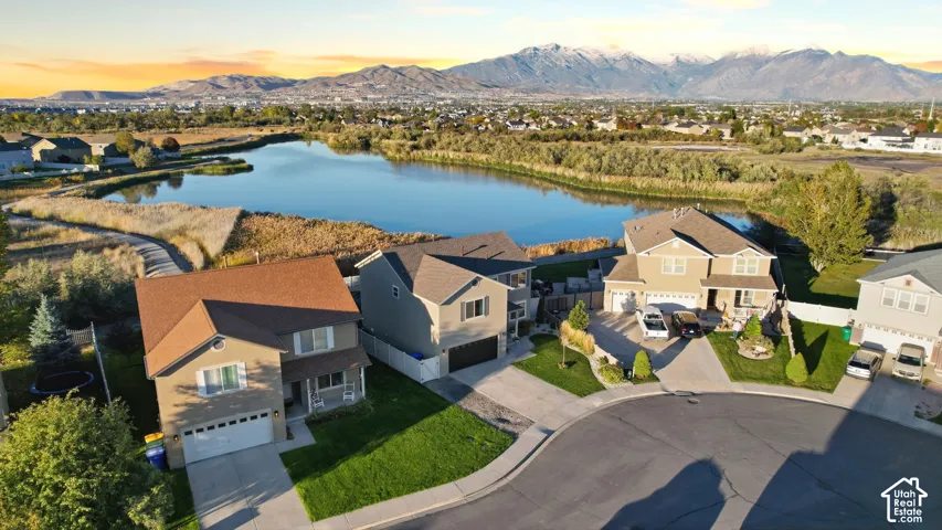 Aerial perspective featuring residential lots with manicured lawns, asphalt driveways, two-story gable-roof construction, and mountain backdrop