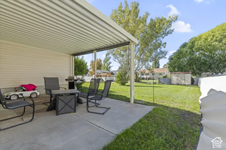 Covered concrete patio with aluminum roofing, expansive lawn, detached storage shed, and perimeter fencing