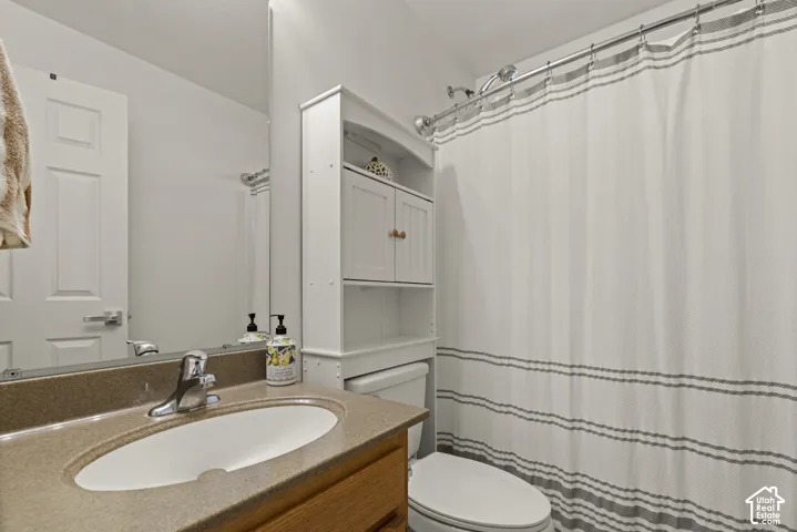 Bathroom featuring a vanity with integrated sink, wood-finish cabinetry, a large wall-mounted mirror, and an over-the-toilet storage unit