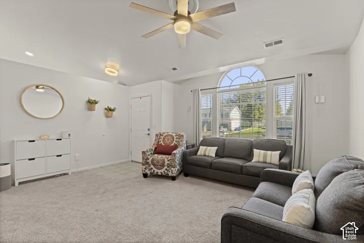 Vaulted ceilings featuring a multi-blade ceiling fan with integrated lighting, oversized arched window, and neutral wall-to-wall carpeting