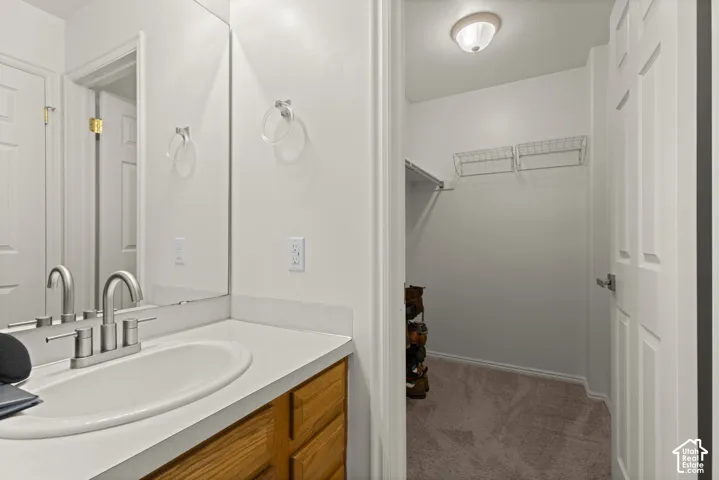 Vanity featuring a stone-composite countertop, undermount oval sink, and satin-finish metal faucet, paired with a walk-in storage area containing wire shelving