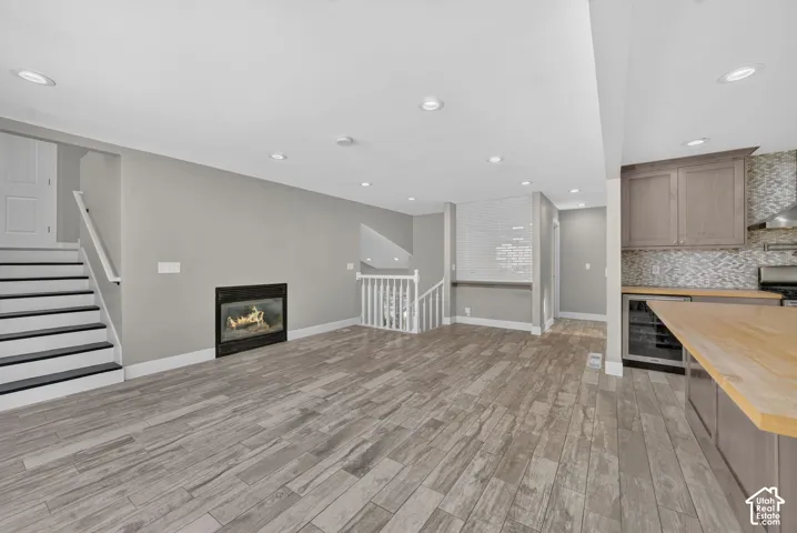 Open-concept room featuring wood-finish tile flooring, a recessed gas fireplace, built-in beverage refrigerator, wood-topped counter, and recessed lighting