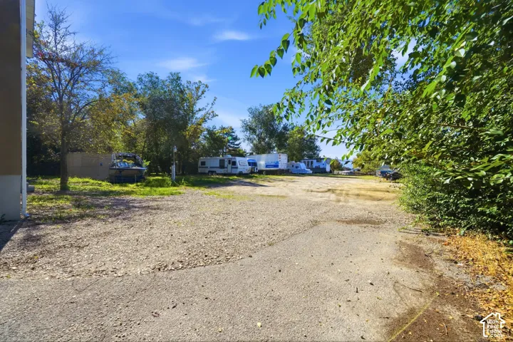 Expansive gravel lot featuring mature trees and established perimeter landscaping