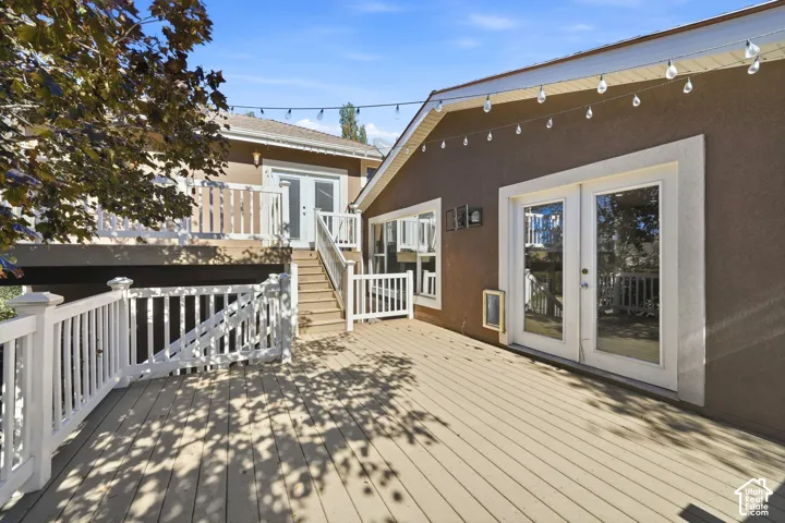 Multi-level wood-finish deck featuring white railings, dual sets of French doors, and overhead string lighting