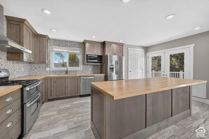 Kitchen featuring wood cabinetry, butcher block countertops, mosaic tile backsplash, stainless steel appliances, and wood-finish flooring