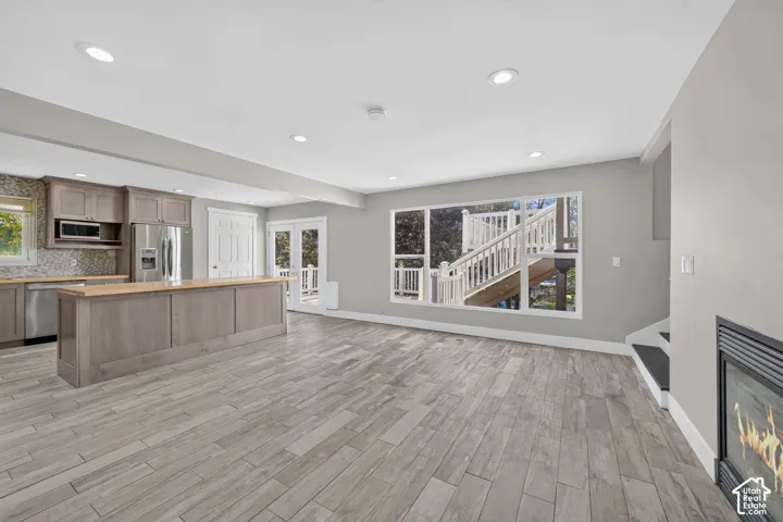 Open-concept space featuring wood-finish flooring, recessed lighting, a center island with a wood-style countertop, stainless steel kitchen appliances, and a wall-mounted fireplace