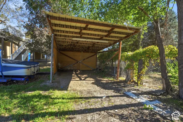 Open-sided carport featuring a corrugated metal roof, timber frame construction, and a crushed gravel surface