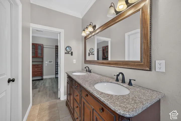 Dual-sink vanity with stone-finish countertop, undermount sinks, and oil-rubbed bronze fixtures, accompanied by a full-width framed vanity mirror, decorative wall-mounted light fixtures, and tiled flooring