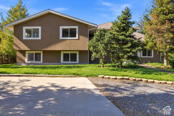 Two-story exterior featuring a stucco facade, gable roofline, multi-pane windows, a paved driveway, and mature landscaping