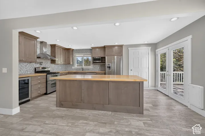 Kitchen featuring shaker-style cabinetry, butcher block island countertop, stainless steel appliances, tiled backsplash, and stone-finish flooring