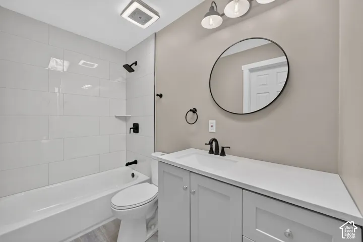 Bathroom featuring a vanity with light-toned cabinetry and a white countertop, subway-tiled tub surround, matte black plumbing fixtures, circular wall mirror, and three-light vanity fixture