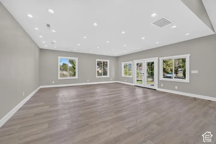 Open-concept interior featuring wood-finish flooring, recessed lighting, double glass-pane doors, and large windows