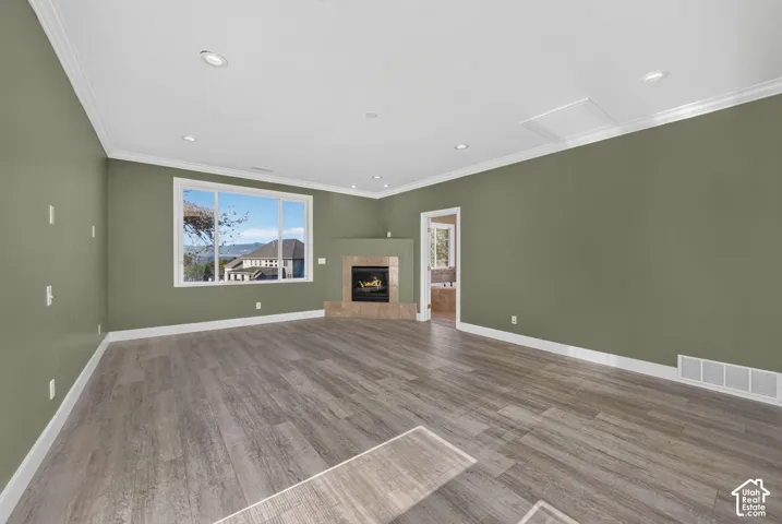 Living space featuring wood-finish flooring, recessed lighting, crown molding, and a corner fireplace with a tiled surround