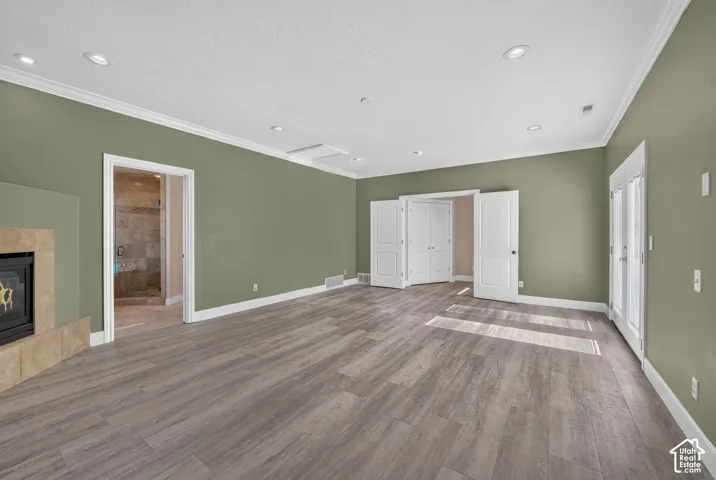 Spacious interior featuring wood-finish flooring, recessed lighting, crown molding, a fireplace with neutral tile surround, and double-door entry