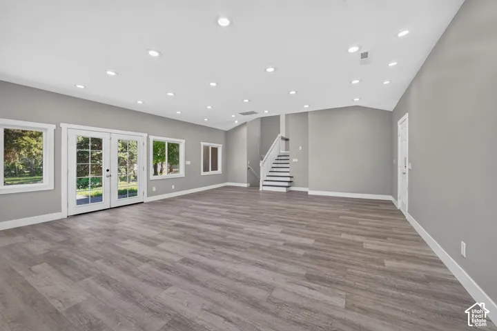 Open-concept interior featuring wood-finish flooring, recessed lighting, expansive glass paneled doors, and a staircase with a white handrail