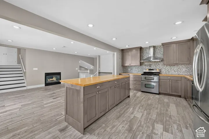 Kitchen featuring wood-finish cabinetry, a central island with a wood countertop, stainless steel appliances, a mosaic tile backsplash, and wood-finish flooring