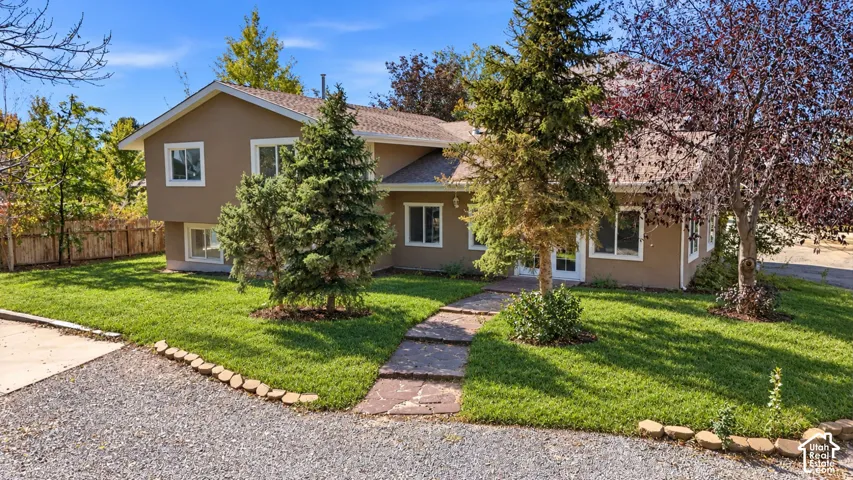 Exterior facade featuring tan siding, a shingled roof, white-trimmed windows, a stone-path walkway, and mature landscaping