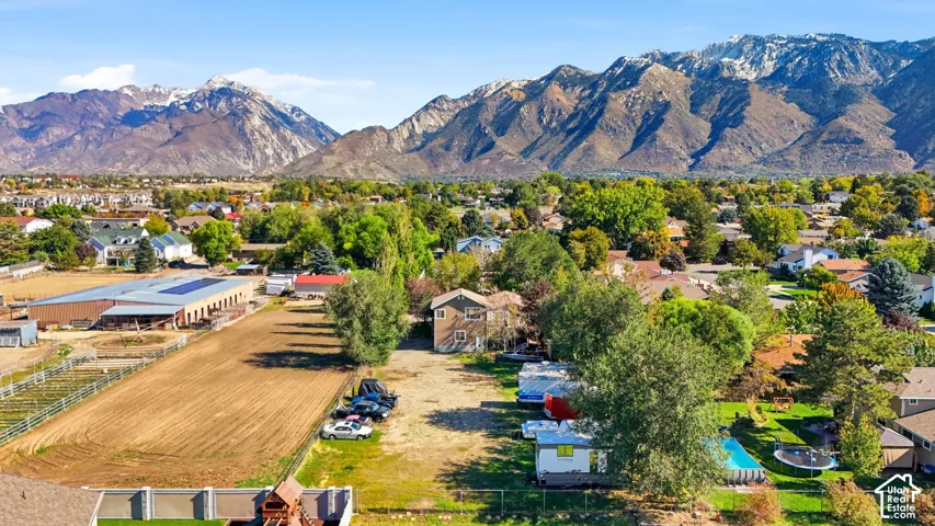 Aerial perspective featuring a multi-acre parcel, perimeter fencing, mature trees, and a mountain backdrop