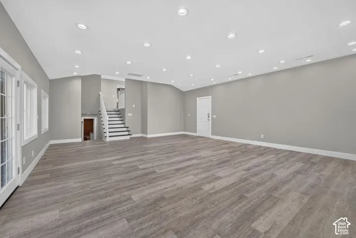 Expansive room featuring wood-finish flooring, vaulted ceilings, recessed lighting, and a staircase with white railings