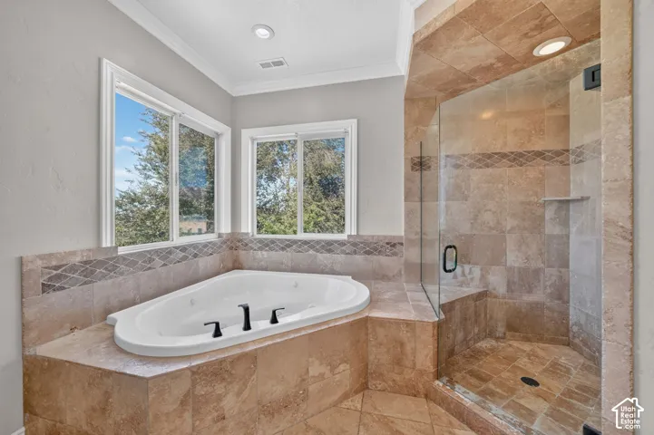 Corner jetted soaking tub with tile surround, walk-in glass-enclosed shower, natural stone tile flooring, and dual sliding windows