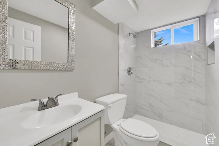 Bathroom featuring a vanity with a white countertop and integrated sink, a walk-in shower with large-format stone-look tile surround, a built-in shower niche, and a horizontal sliding window