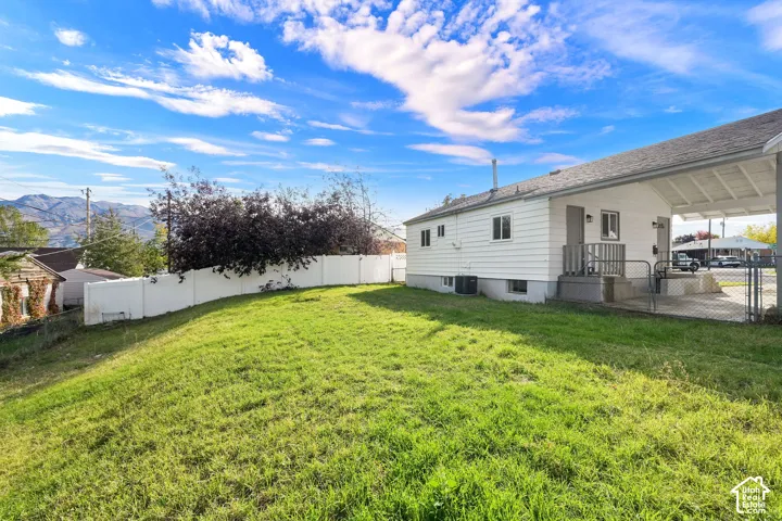 Backyard featuring a grass lawn, white vinyl privacy fencing, and a covered carport with mountain backdrop