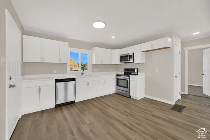Kitchen featuring white cabinetry, stainless steel appliances, wood-finish flooring, and solid surface countertops
