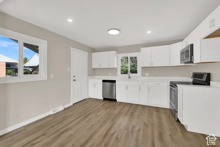 Kitchen featuring white shaker-style cabinetry, stainless steel appliances, wood-finish flooring, recessed lighting, and solid-surface countertops