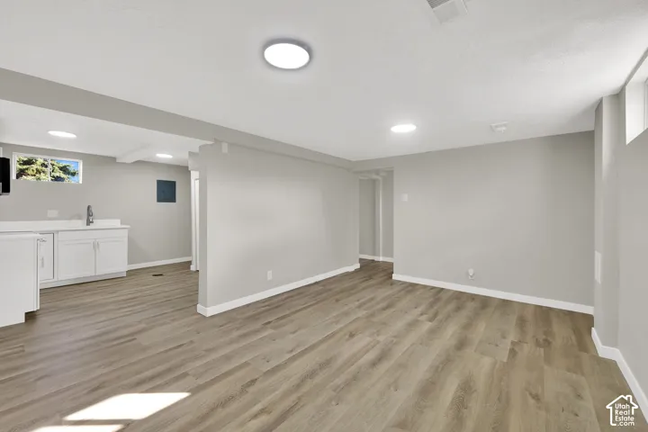 Open-concept area featuring wood-finish flooring, recessed lighting, and a kitchenette with white cabinetry and a sink
