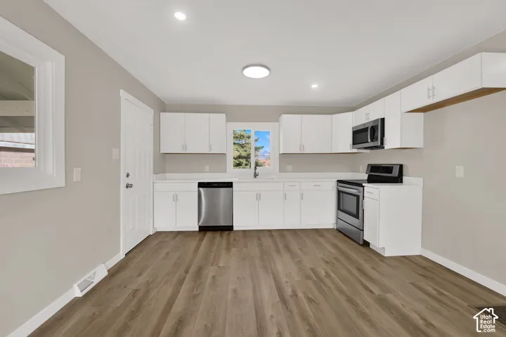 Kitchen featuring white cabinetry, wood-finish flooring, stainless steel appliances, and solid-surface countertops