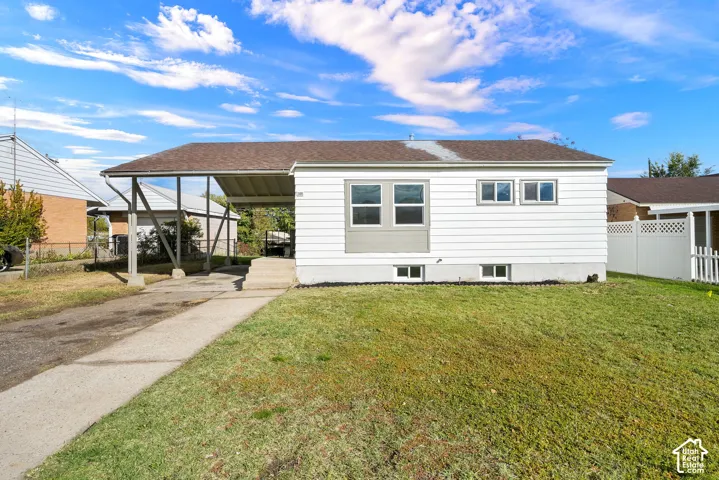 Single-story exterior featuring white horizontal siding, a covered carport, an asphalt shingle roof, concrete driveway, and a front lawn
