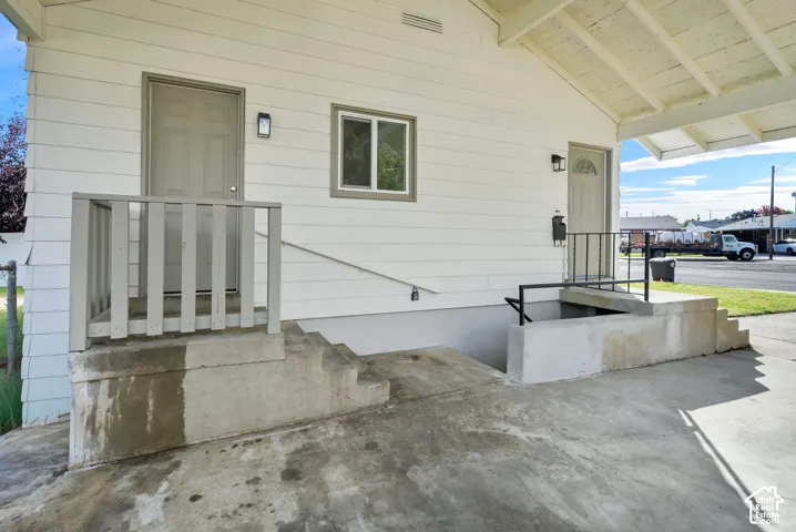Exterior featuring white horizontal siding, a covered concrete porch, concrete stairs with metal handrails, and two separate exterior entry doors