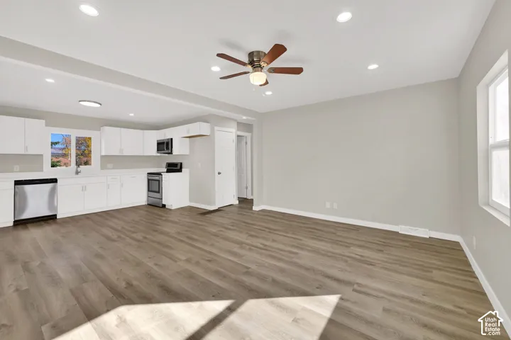 Open-concept interior featuring wood-finish flooring, recessed lighting, white cabinetry, stainless steel kitchen appliances, and a ceiling fan