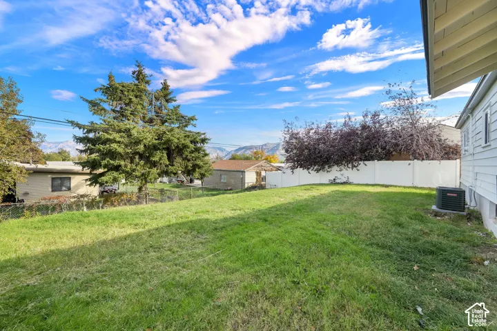 Open backyard featuring a manicured lawn, mature trees, mountain backdrop, and privacy fencing