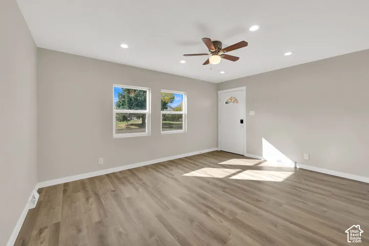 Neutral-toned interior featuring wood-finish flooring, recessed lighting, a ceiling fan with integrated light, and a white entry door with a decorative glass insert