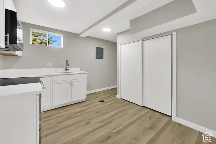 Kitchenette featuring white cabinetry, solid-surface countertops, an integrated sink with a gooseneck faucet, wood-finish flooring, and a sliding-door closet