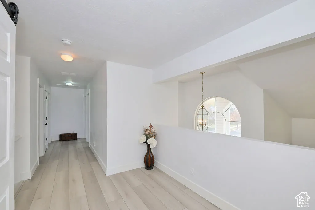 Hallway featuring wood-finish flooring, recessed ceiling lighting, a half-wall partition, and a decorative arched window with a suspended lantern-style pendant fixture
