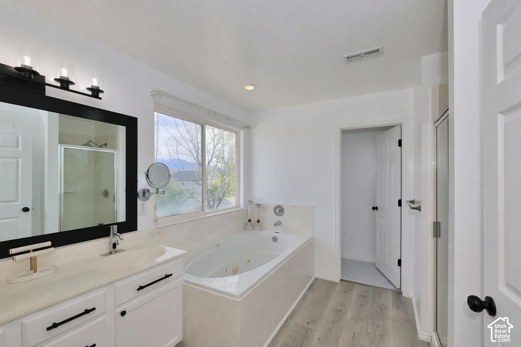 White vanity with a rectangular sink, jetted soaking tub with tile surround, wood-finish flooring, and black hardware accents